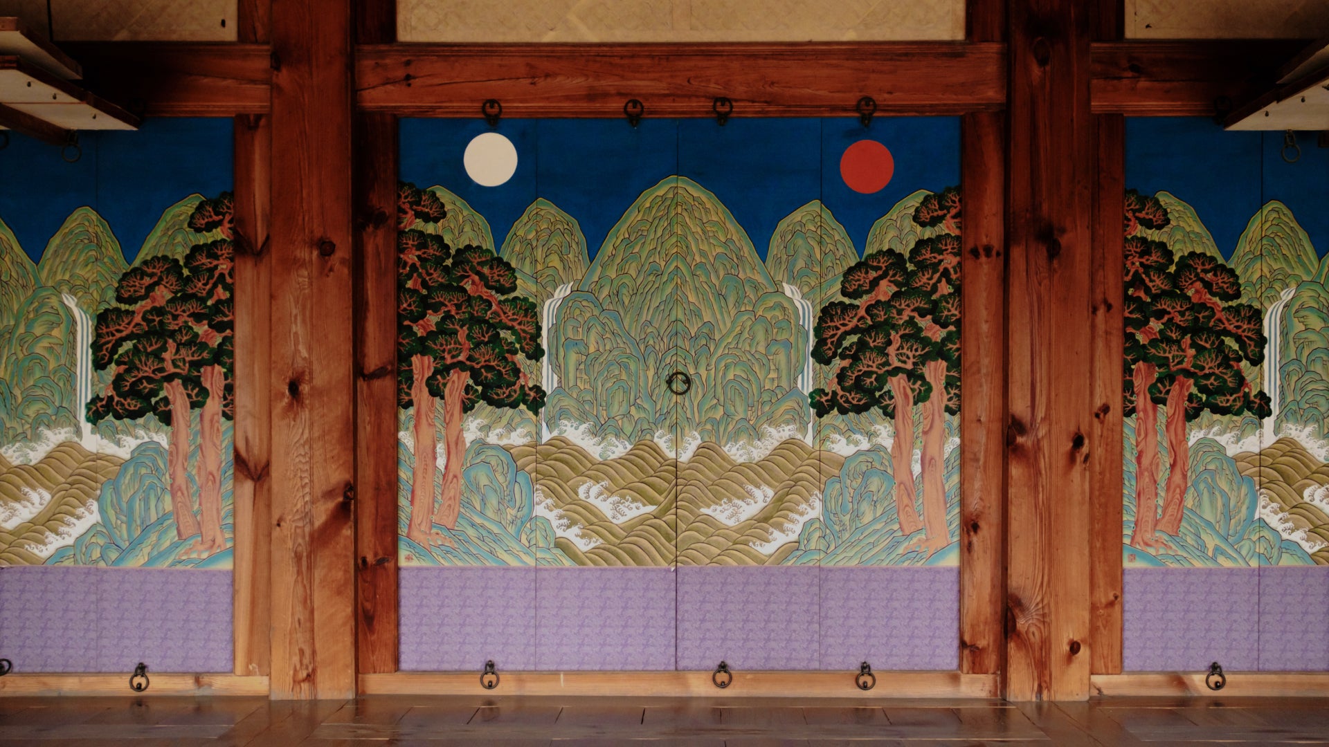 Traditional Korean wooden door with colorful paintings of mountains, trees, and celestial symbols representing harmony in nature.