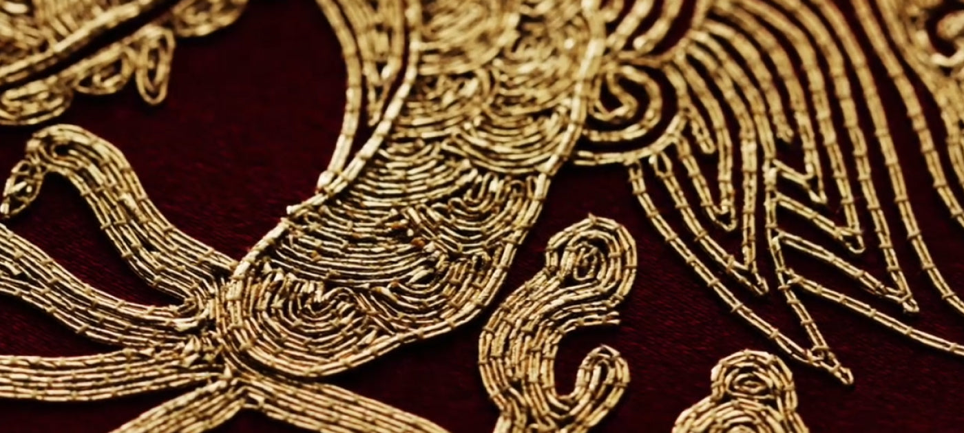 A detailed view of a phoenix embroidered in gold on deep red fabric.